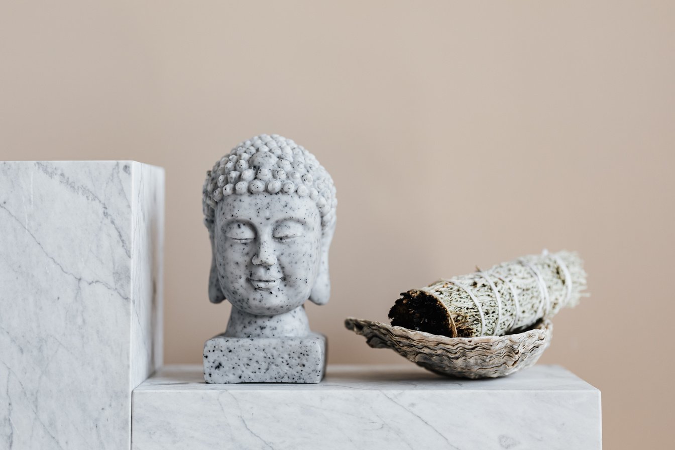 Stone Buddha and sage incense bundle in bowl on marble shelf